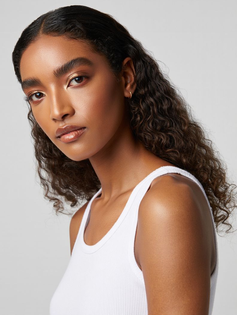 Aisha — AI fashion model: Long curly hair, gold earring, warm presence