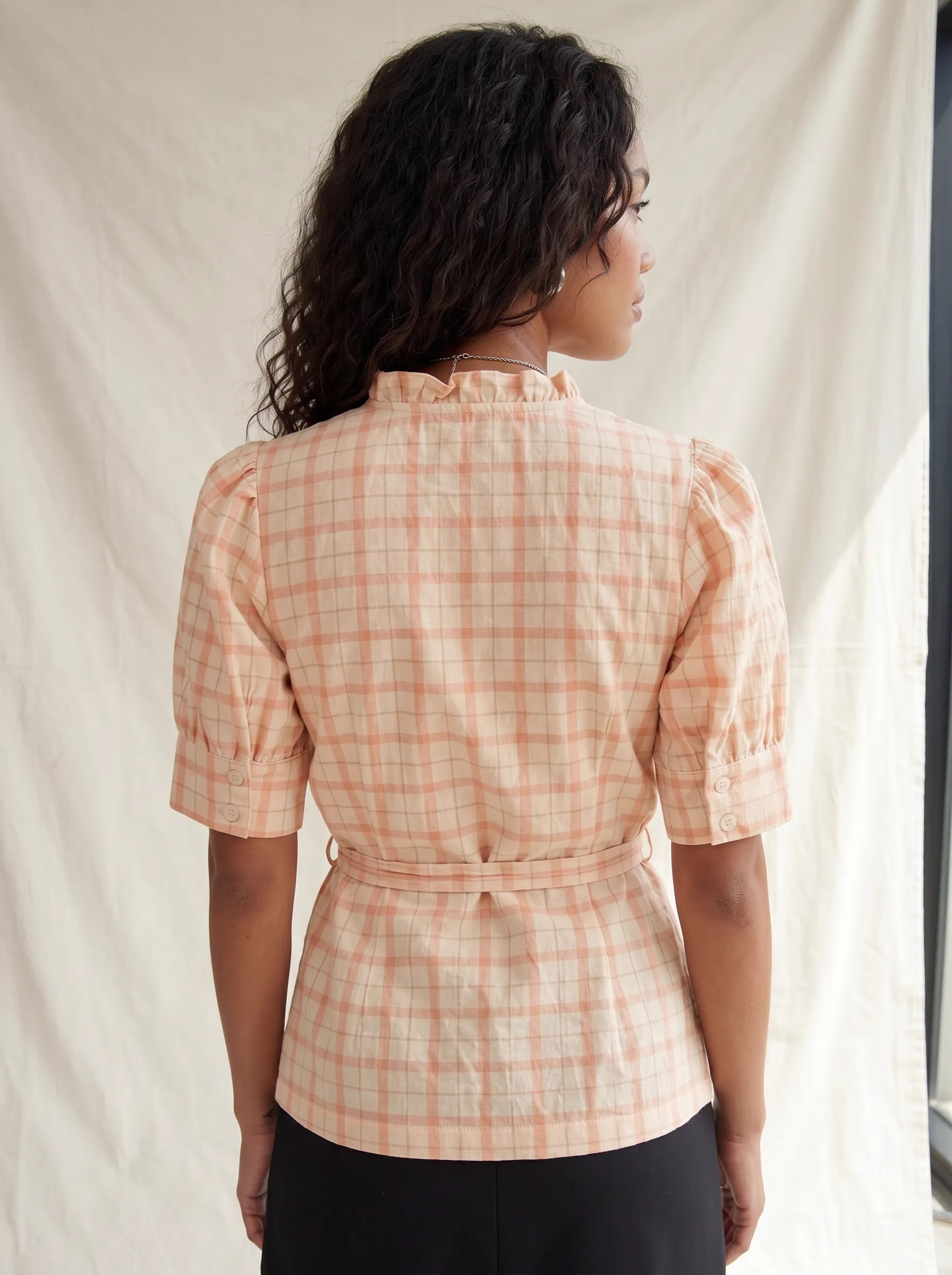 MODA AI output 3 — full-body studio model wearing peach plaid wrap top with belt and ruffle detail