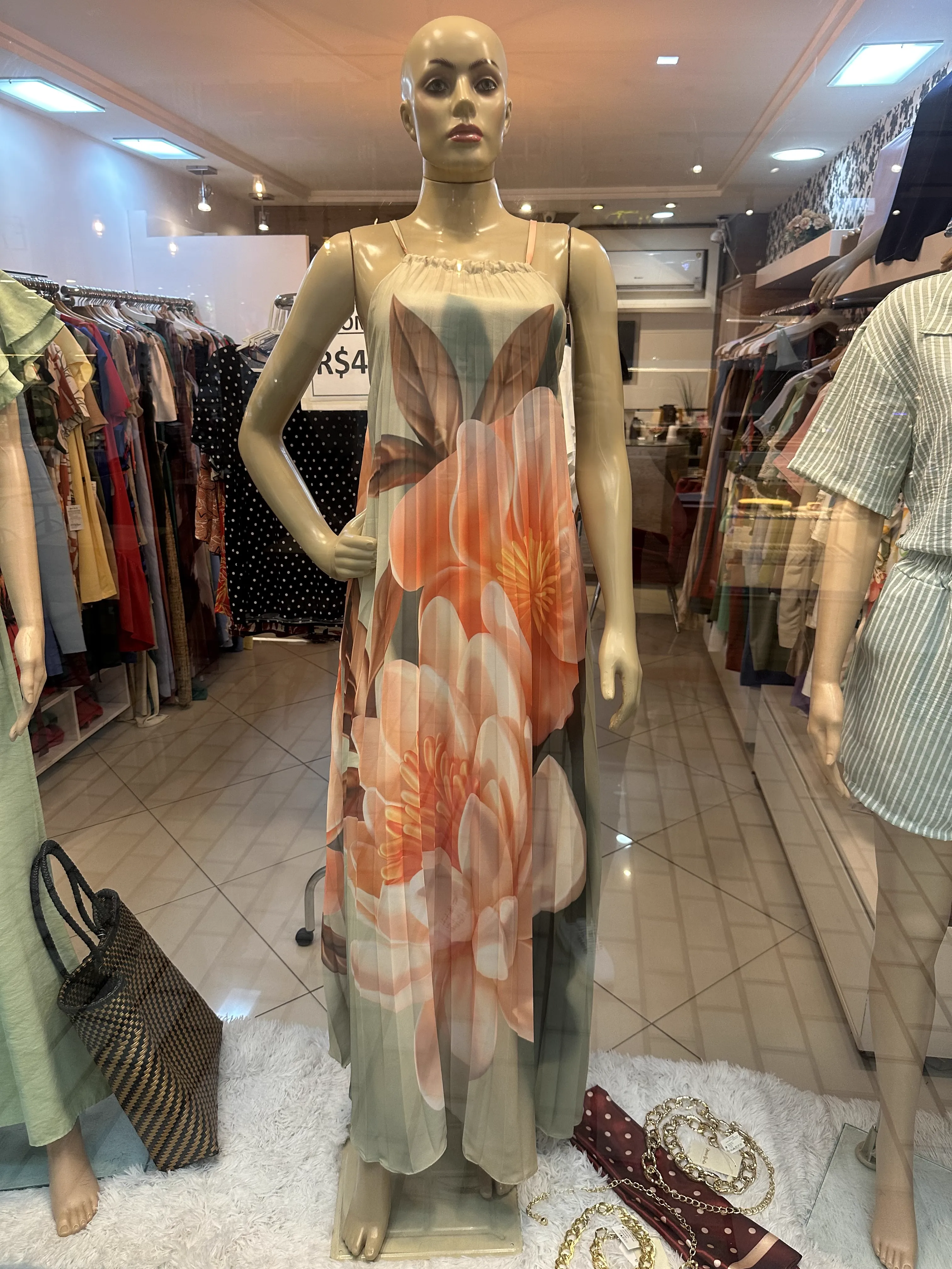 Shop mannequin reference photo — sideways phone snap of floral pleated sundress on display mannequin under fluorescent shop lighting with surrounding clutter