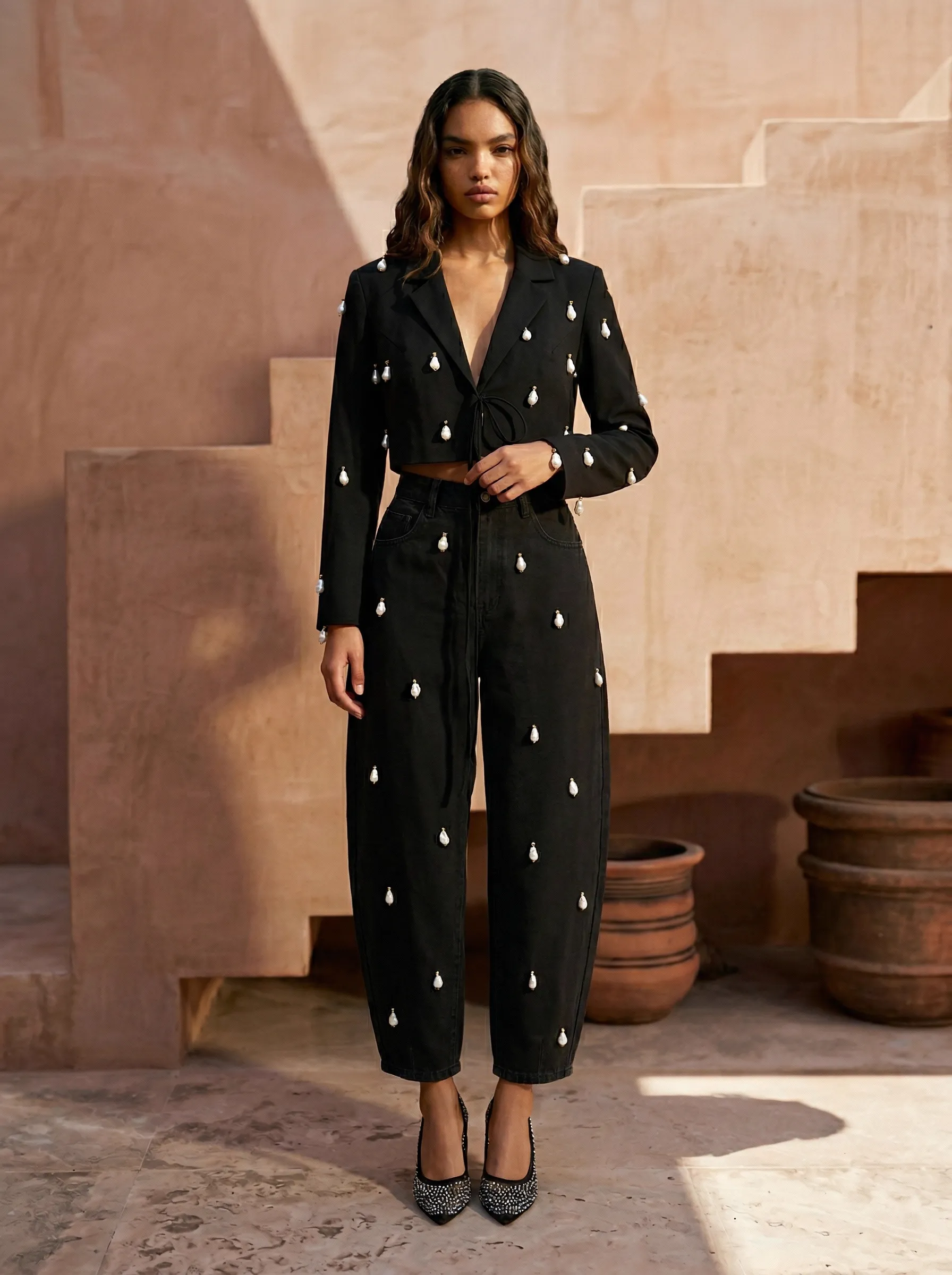 MODA AI resortwear output — black cropped blazer and barrel-leg jeans with pearl embroidery on terracotta adobe staircase